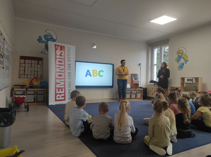 Dzieci siedzą na podłodze i słuchają jak Pani opowiada o segregacji odpadów