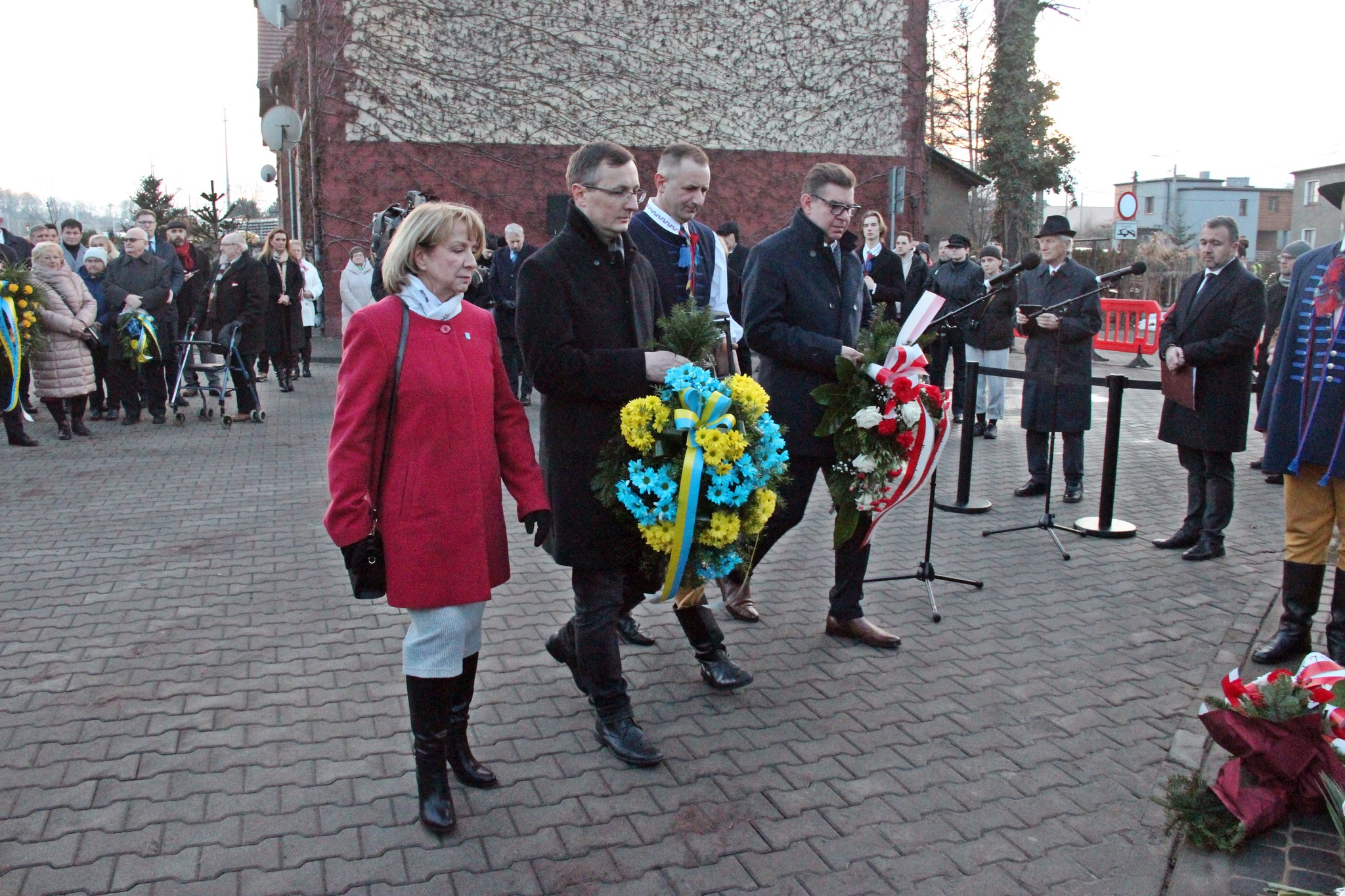 Cztery osoby składają wieńce przed tablicą pamiątkową