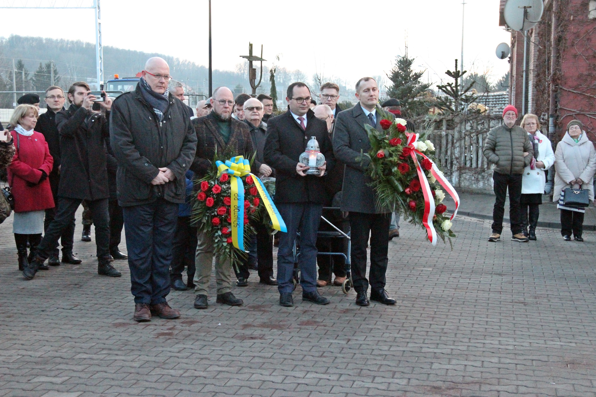 Czterech panów stoi z wieńcami i zniczem